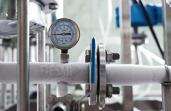 Frozen industrial pipe with DESMI pressure gauge, indicating fluid handling system conditions.