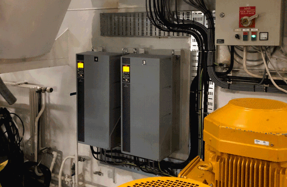 Industrial equipment room with control panels, wiring, and large yellow machinery.