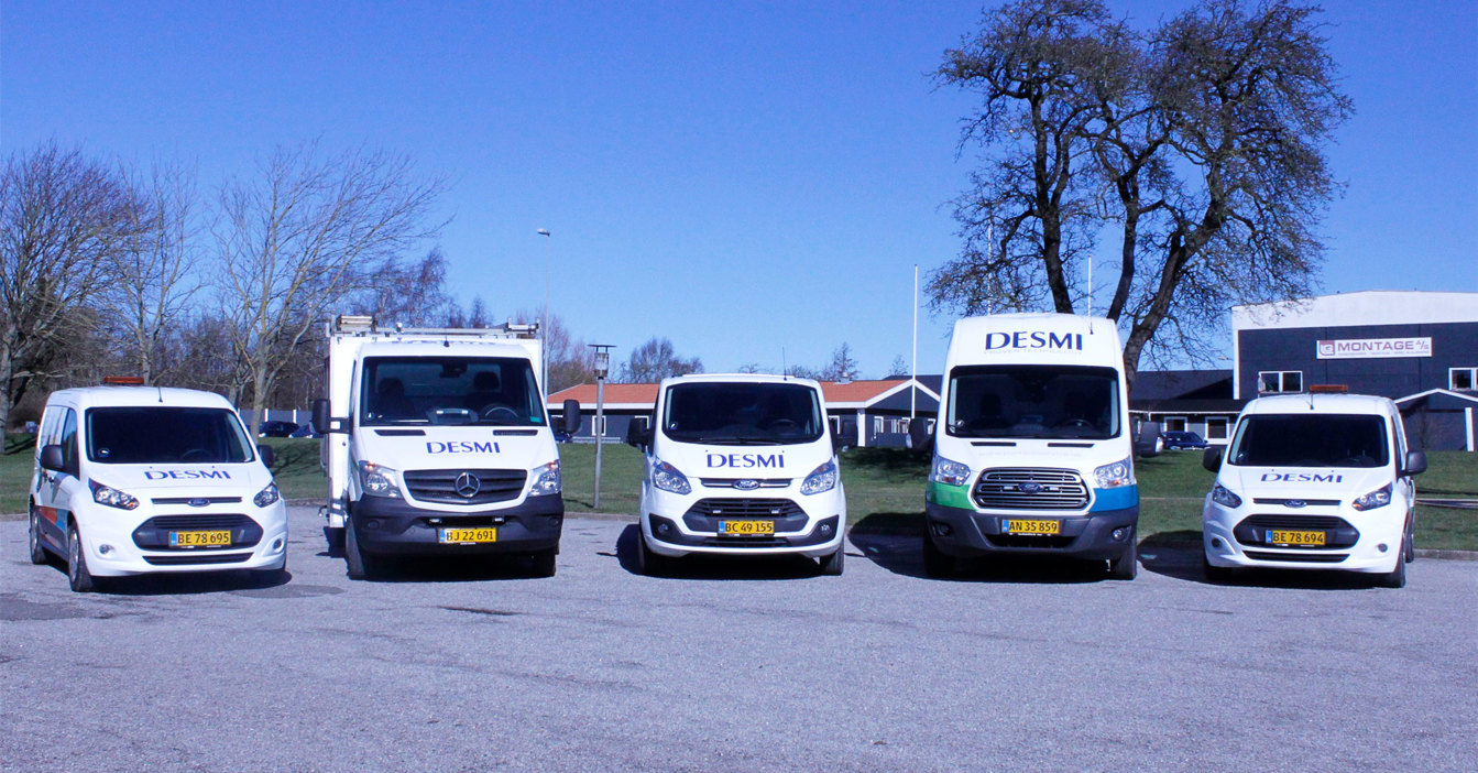 Five DESMI-branded vans parked in a row under a clear blue sky.