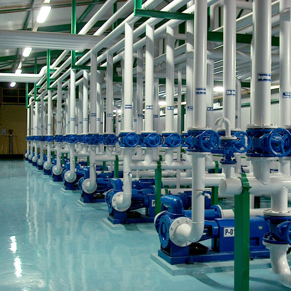 Industrial facility with multiple blue pumps and white pipes for fluid handling.
