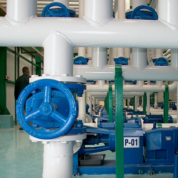 Industrial pumps and blue valves connected to white pipes in a facility.