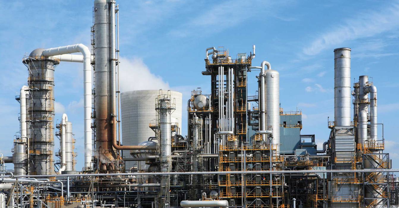 Industrial plant with numerous pipes and towers under a clear blue sky.