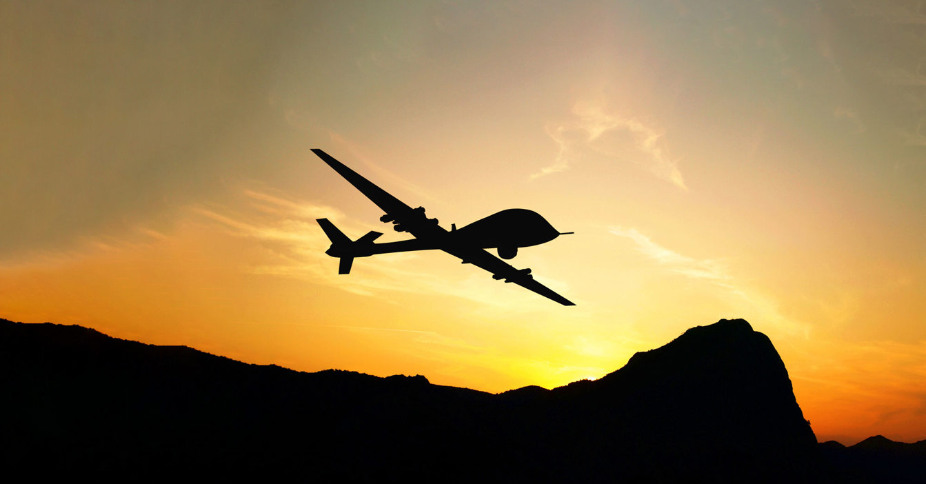 Silhouette of a drone flying over mountains during a golden sunset.