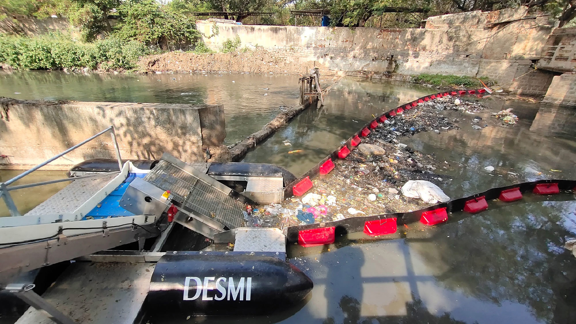 DESMI system collecting debris from a polluted river using a floating barrier.