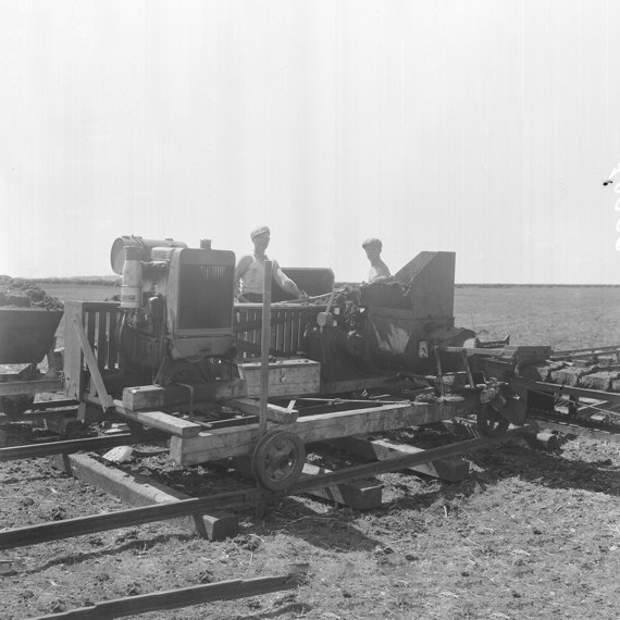 Two men operating a machine on wooden tracks in a field.
