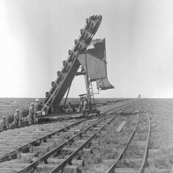 Construction workers using machinery to lay railroad tracks in a barren landscape.
