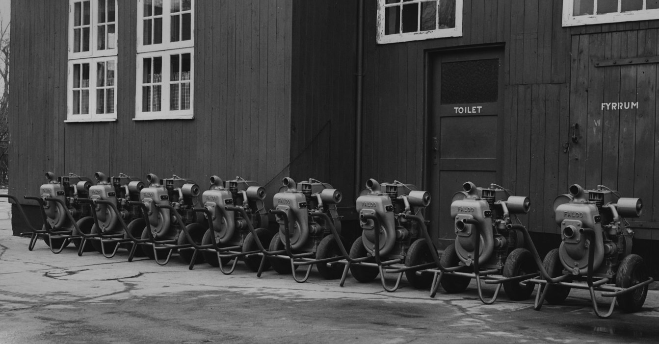 Row of portable pumps lined up against a wooden building.