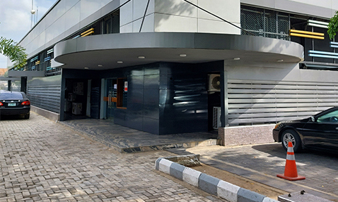 Modern building entrance with sleek design, parked cars, and an orange traffic cone.