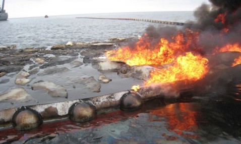 Oil spill containment with burning flames on the water surface.
