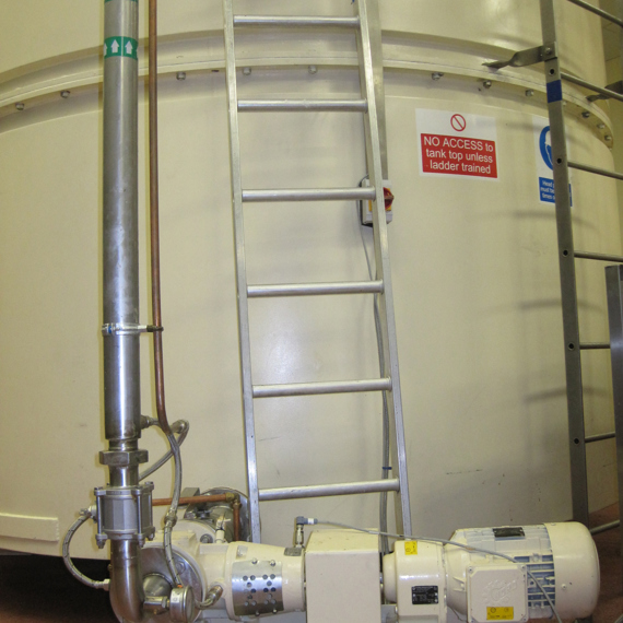 Industrial tank with a ladder, pump, and safety signage about ladder training.