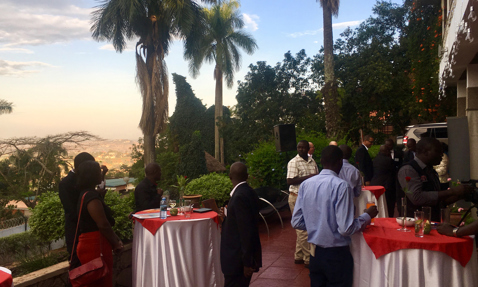 Outdoor gathering with people socializing at tables under palm trees.