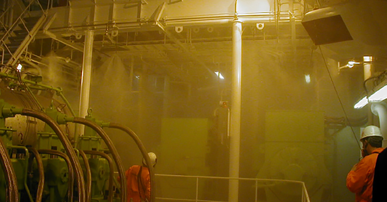 Área industrial con trabajadores en equipo de protección en medio de una densa niebla y maquinaria.