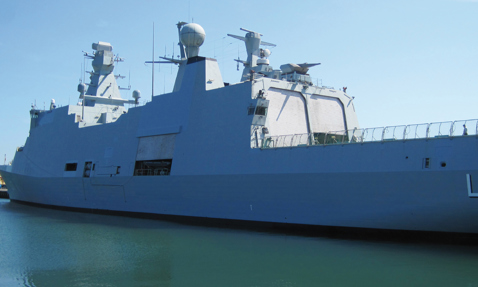 Navy warship docked at a calm harbor under a clear blue sky.