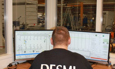 Person in DESMI shirt monitors fluid handling system on dual screens.