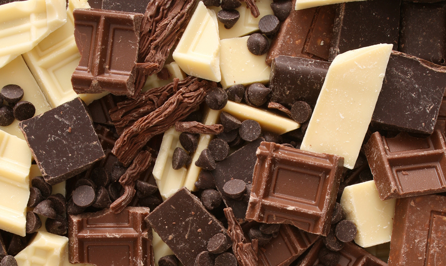 Blandade bitar av vit, mjölk- och mörk choklad med chokladchips i en hög.