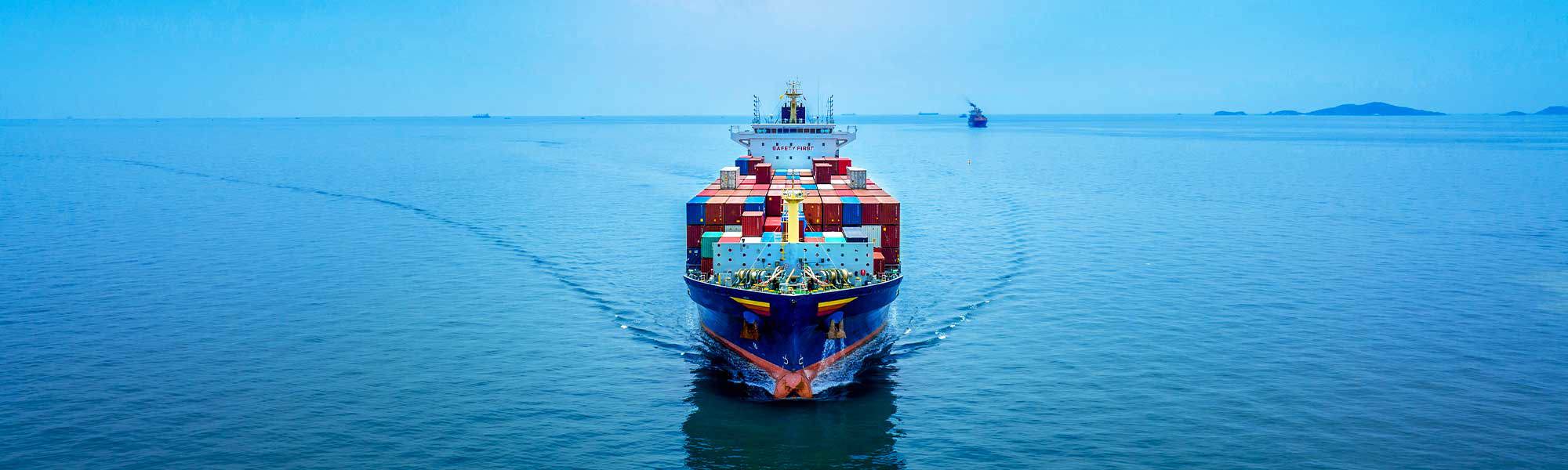 Container ship sailing on a calm ocean under a clear blue sky.