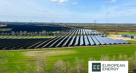 Solar farm with rows of panels and wind turbines in the distance. European Energy logo.