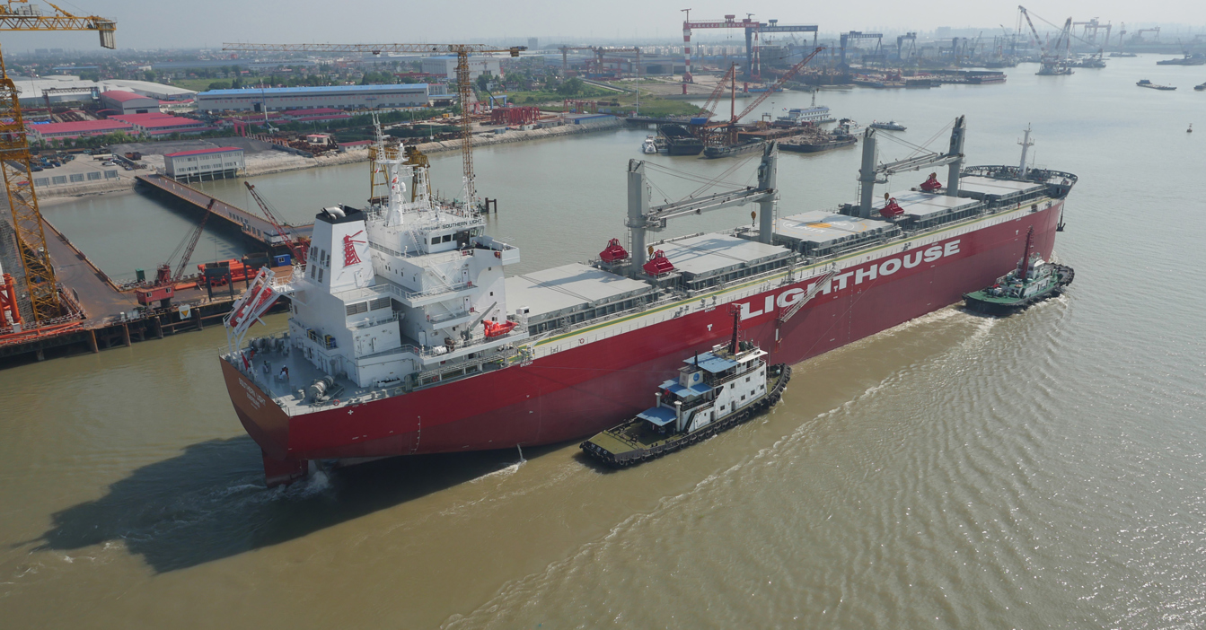 Large red cargo ship "Lighthouse" assisted by tugboats in a busy shipyard.