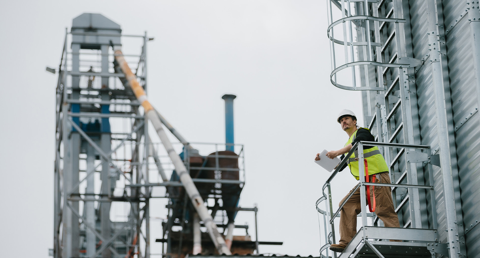 Travailleur de la construction en équipement de sécurité inspecte un site industriel depuis une plateforme surélevée.