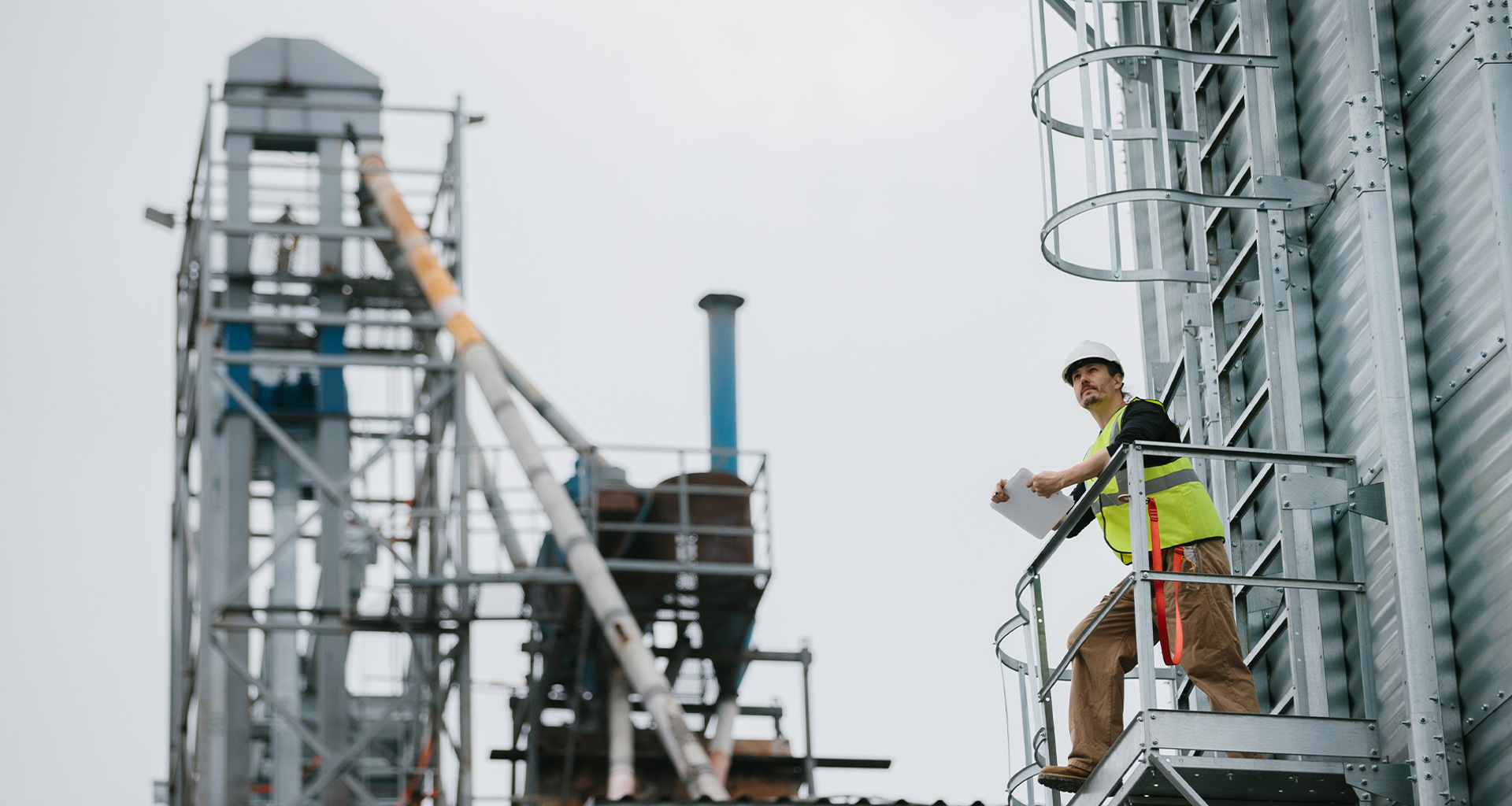 Travailleur de la construction en équipement de sécurité inspecte un site industriel depuis une plateforme surélevée.