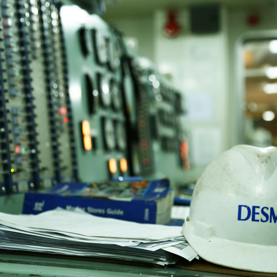 Casque de sécurité DESMI sur le bureau du panneau de contrôle dans un environnement industriel.
