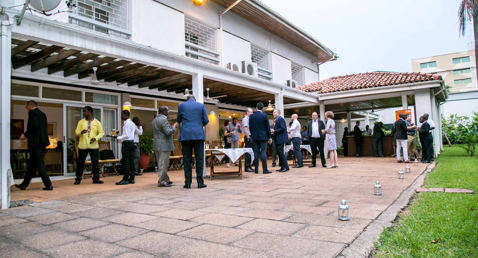 People socializing at an outdoor event near a building with a tiled roof.