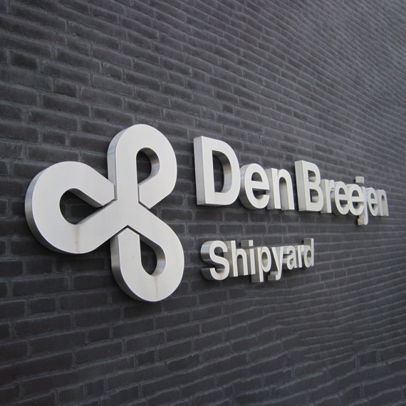 Den Breejen Shipyard logo on a dark brick wall background.