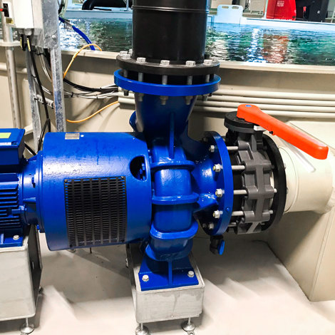 Blue industrial pump system near a large water tank for fluid handling.
