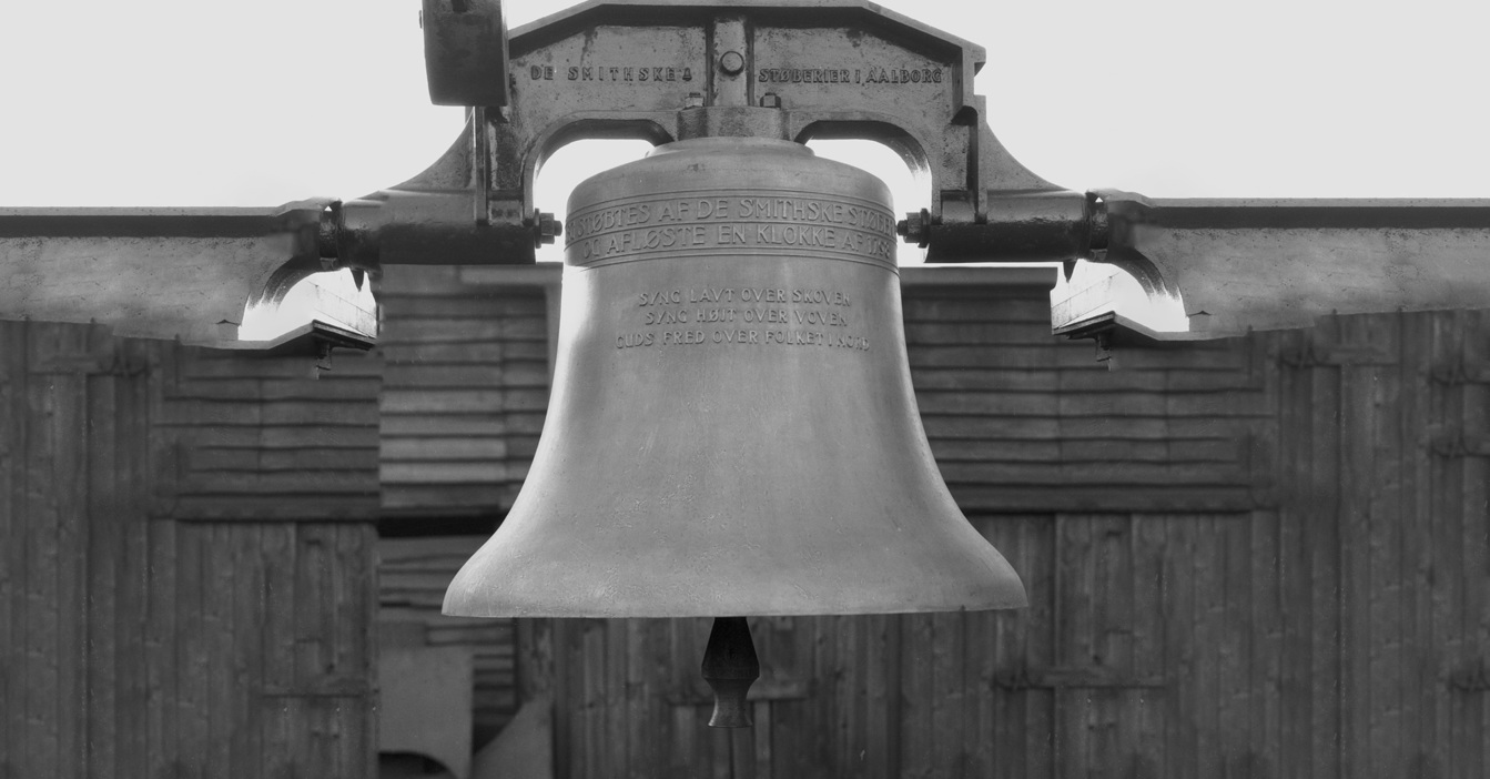 Large metal bell with inscriptions, mounted on a wooden structure in monochrome.