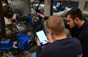 Two technicians examine industrial equipment with a tablet for fluid handling maintenance.