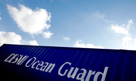 Blue container labeled "DESMI Ocean Guard" against a cloudy sky background.