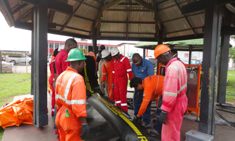 Workers in safety gear inspecting equipment under a shelter at an outdoor site.