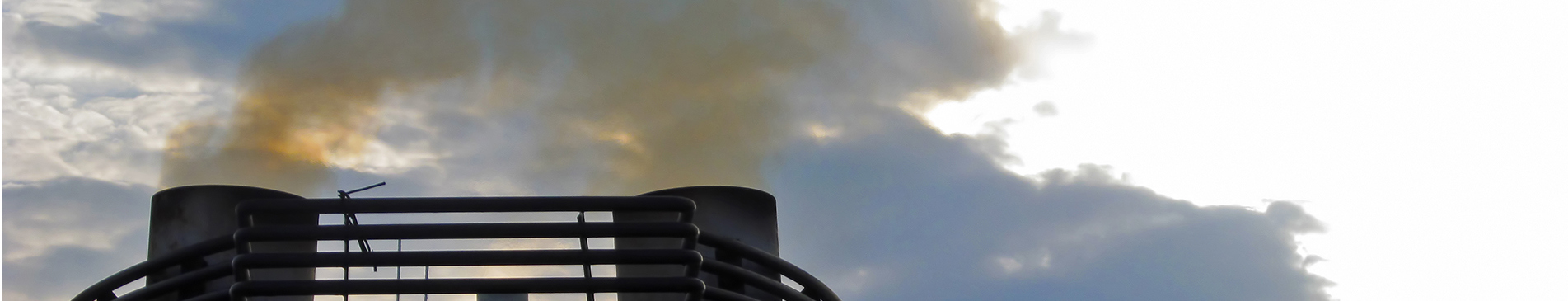 Industrial smoke stacks emitting fumes against a cloudy sky.