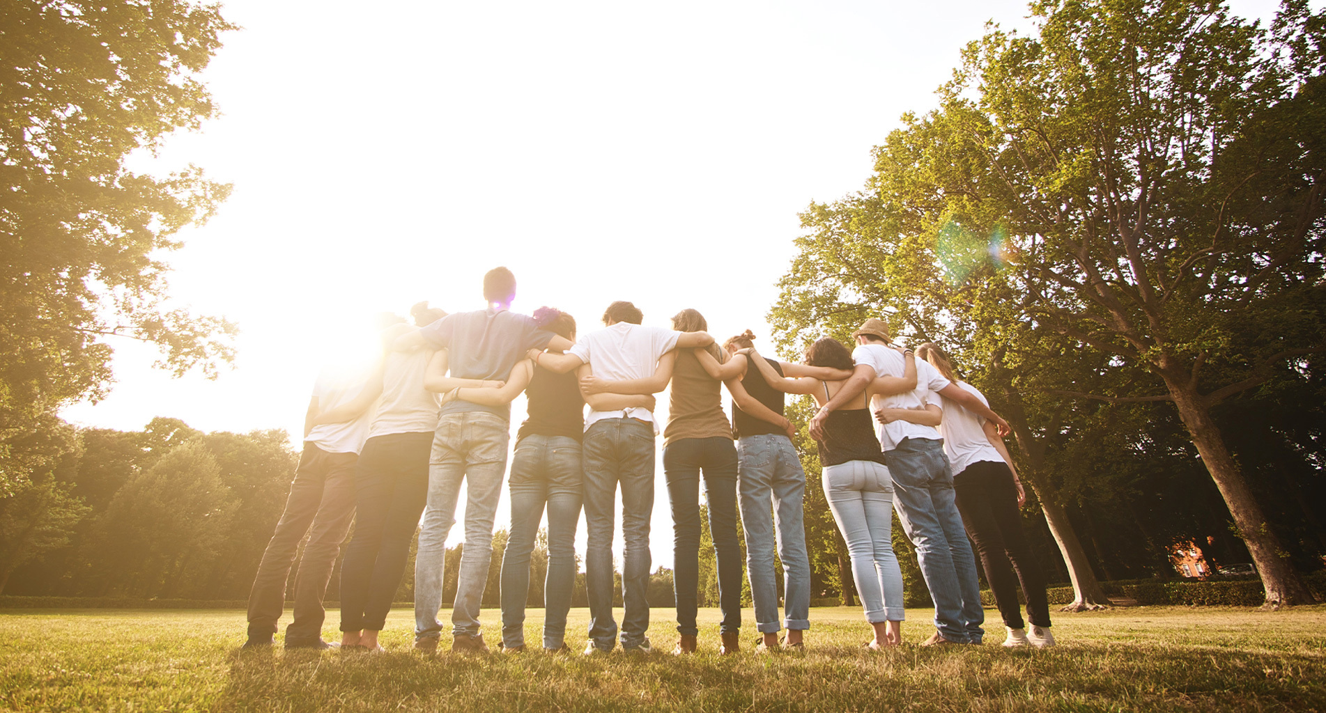 Group of people embracing outdoors under a bright sunlit sky.