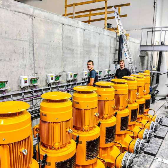 Two workers beside a row of yellow DESMI pumps for fluid handling.