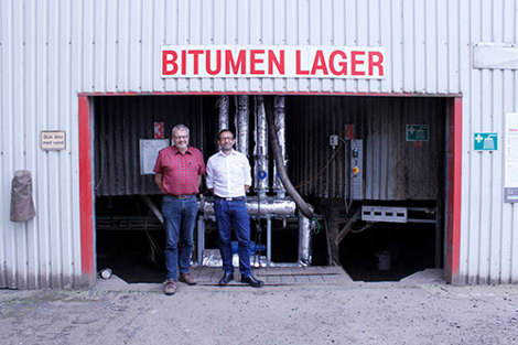Two men standing in front of a bitumen storage facility entrance.