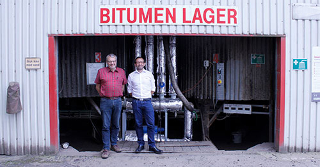 两名男子站在沥青储存设施入口前。