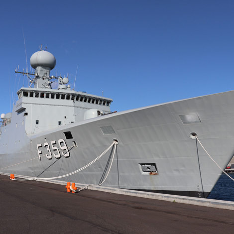 A naval ship docked at a pier, displaying the Danish flag.