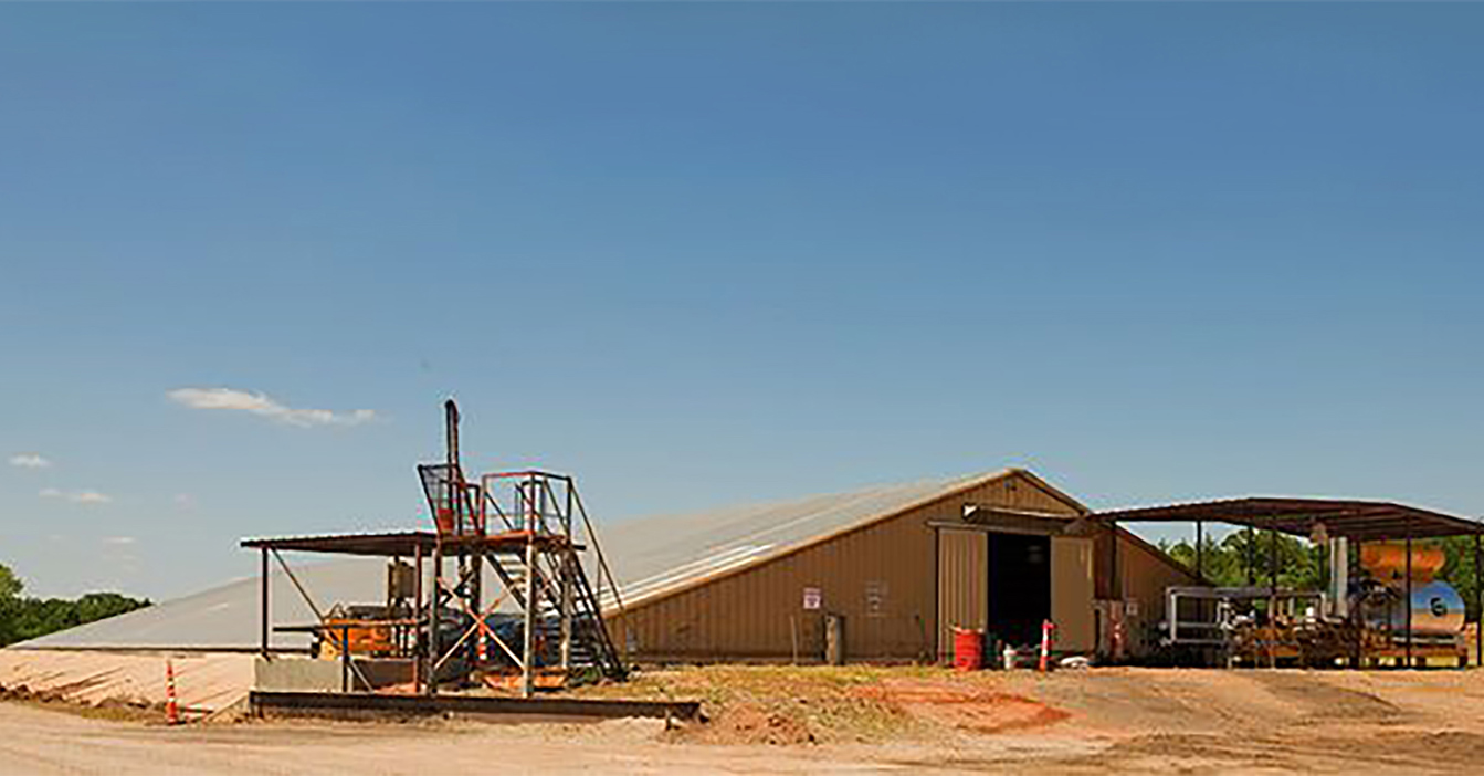 Industrial building with metal framework and equipment under a clear blue sky.
