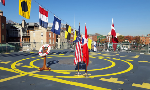 船甲板上的旗帜和“Peter Willemoes”救生圈，背景是建筑物。