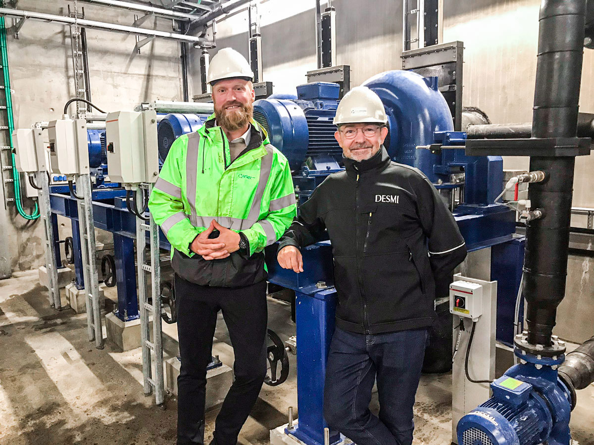 Two men in hard hats stand by DESMI industrial pumps in a facility.