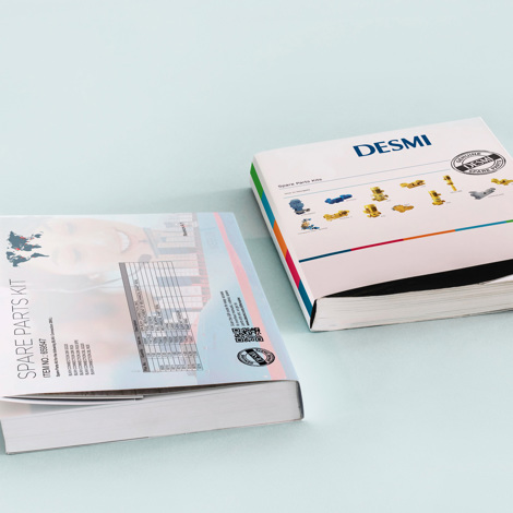 Två DESMI reservdelskataloger på en ljusblå yta.