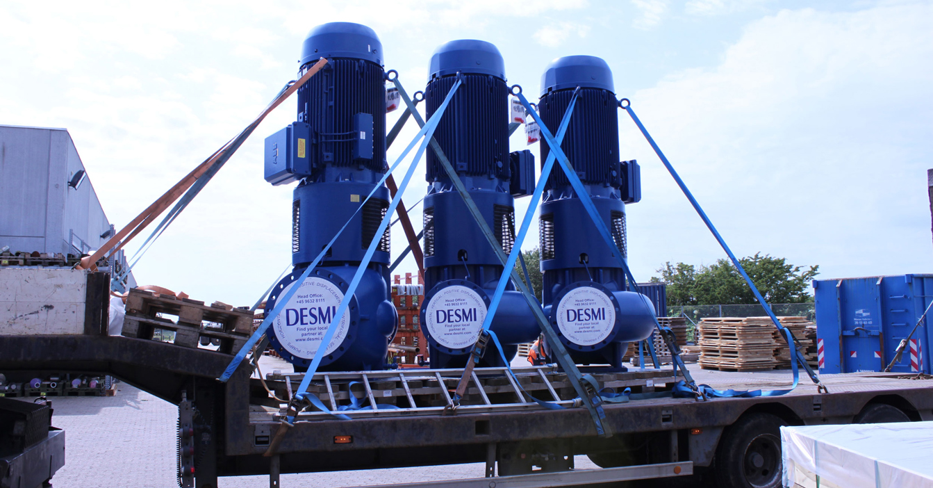 Three large blue DESMI pumps secured on a flatbed trailer for transport.