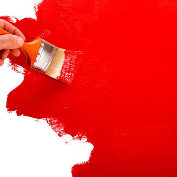 Hand painting a wall red with a paintbrush, leaving a smooth finish.