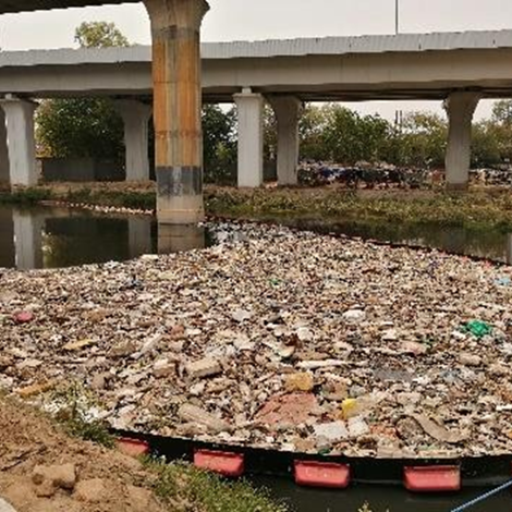 Floating barrier traps large amount of trash in river under highway bridge.