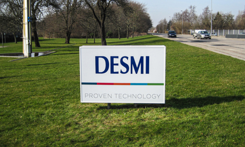 草地上的DESMI标志，背景是树木和道路。