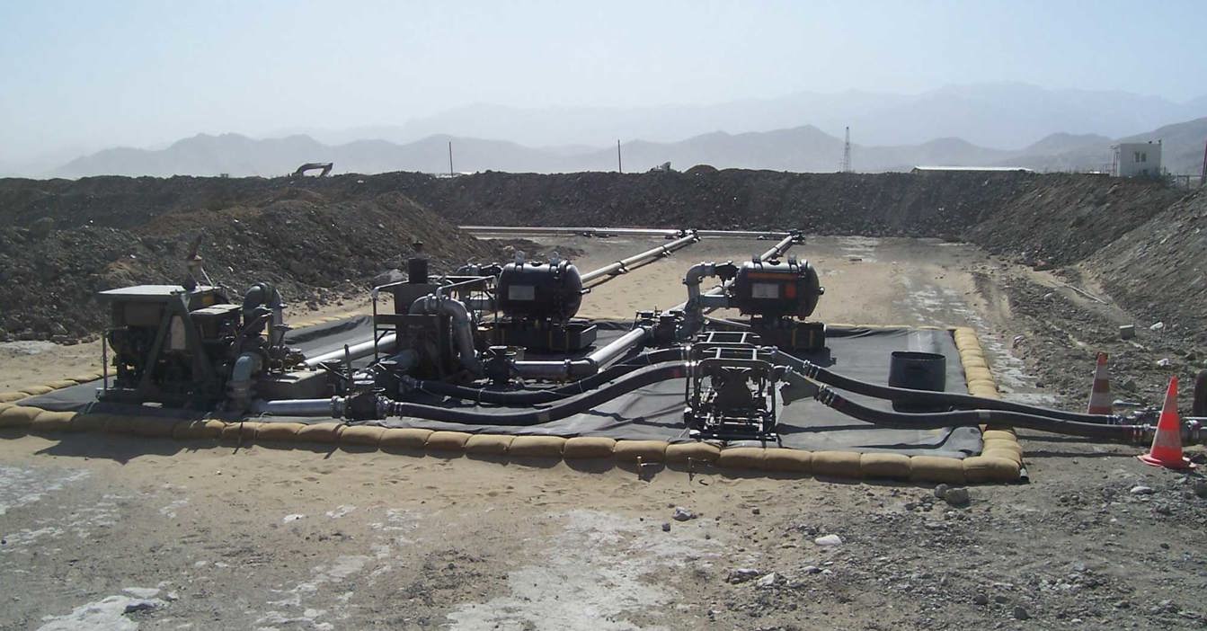 Industrial pumps and pipes on a construction site with mountainous background.