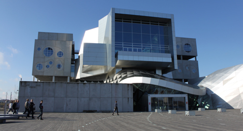 Modern architectural building with geometric designs and people walking in the foreground.