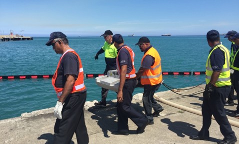 工人在阳光明媚的日子里穿着安全背心在海洋附近操作设备。