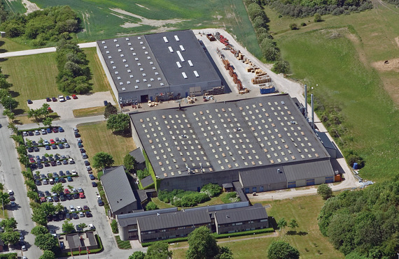 Aerial view of an industrial facility with parking and surrounding greenery.